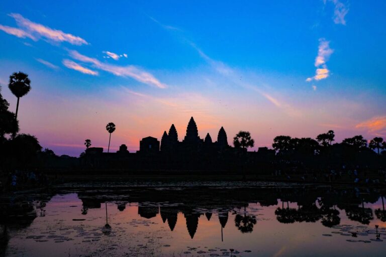 Angkor Wat silhouetted against a pink dawn sky and reflected in water