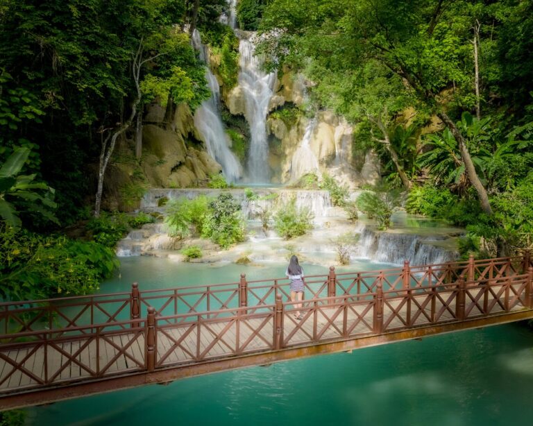 Tiered waterfall and wooden footbridge above turquoise water in a forest in Laos