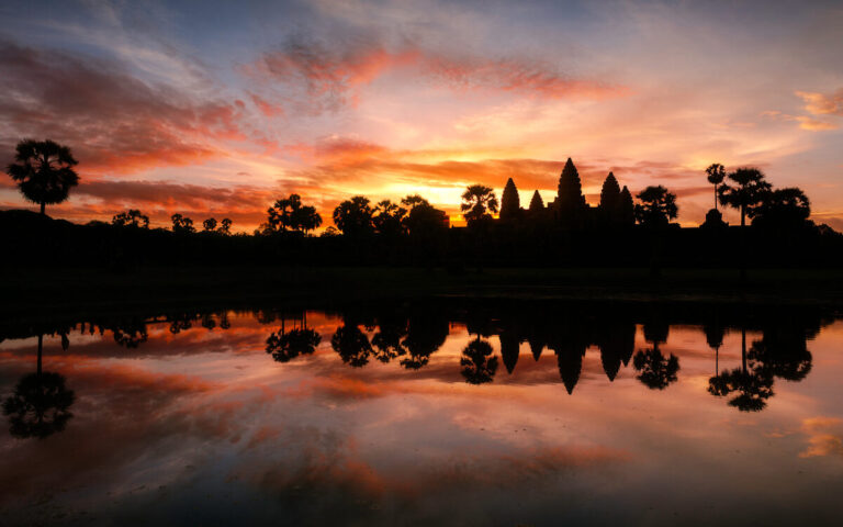 Angkor Wat reflected in water beneath an orange sunrise sky