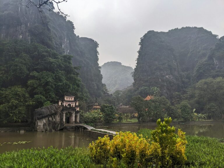 Temple gateway beside water and limestone cliffs in Ninh Binh, Vietnam