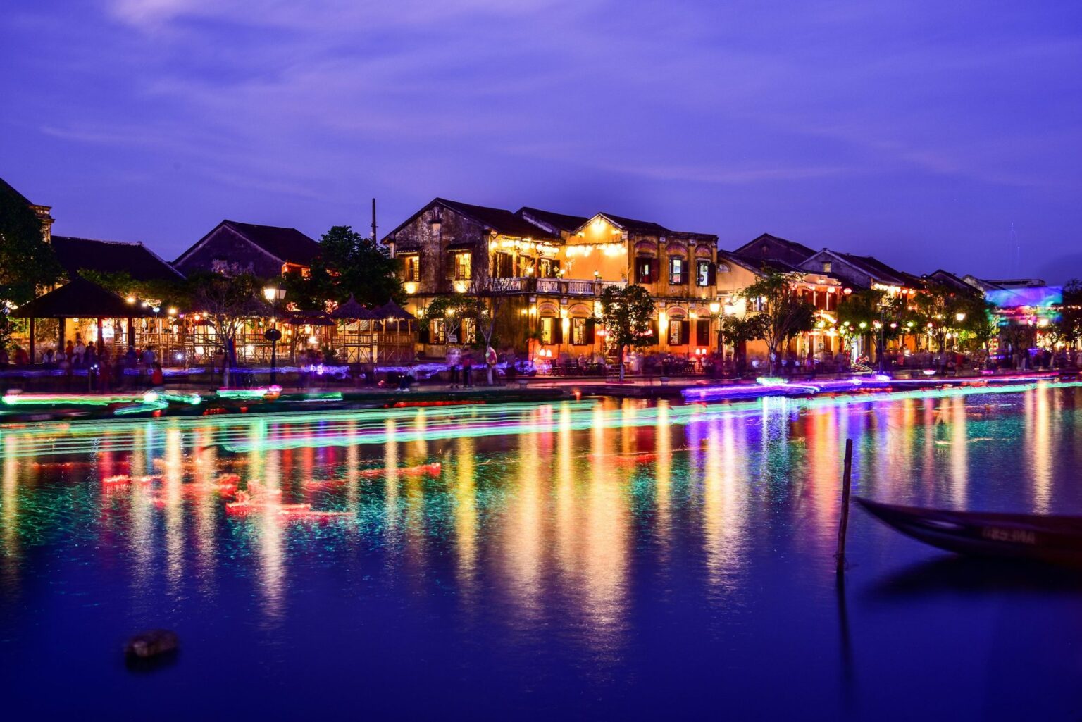 Illuminated riverside buildings and colourful reflections on the river in Hoi An at dusk